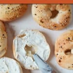 top down view of several bagels with one cut in half and spread with cream cheese