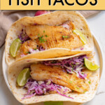 Two fish tacos garnished with lime wedges on a plate.