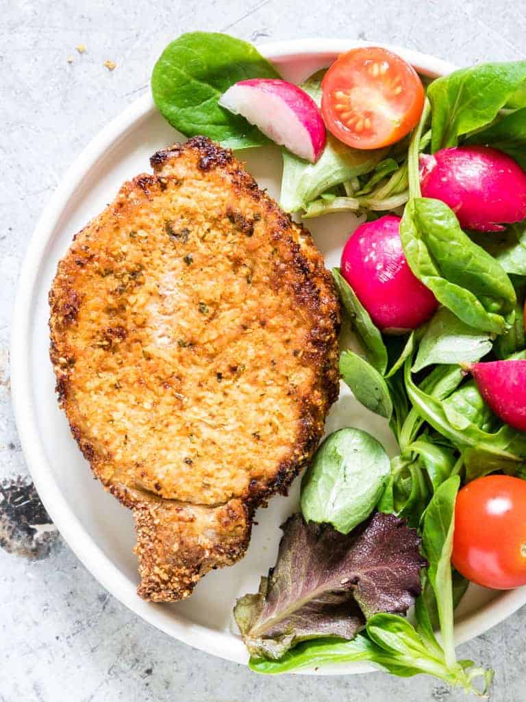 One serving of Air Fryer Pork Chops on a white dinner plate served with fresh greens and tomato salad