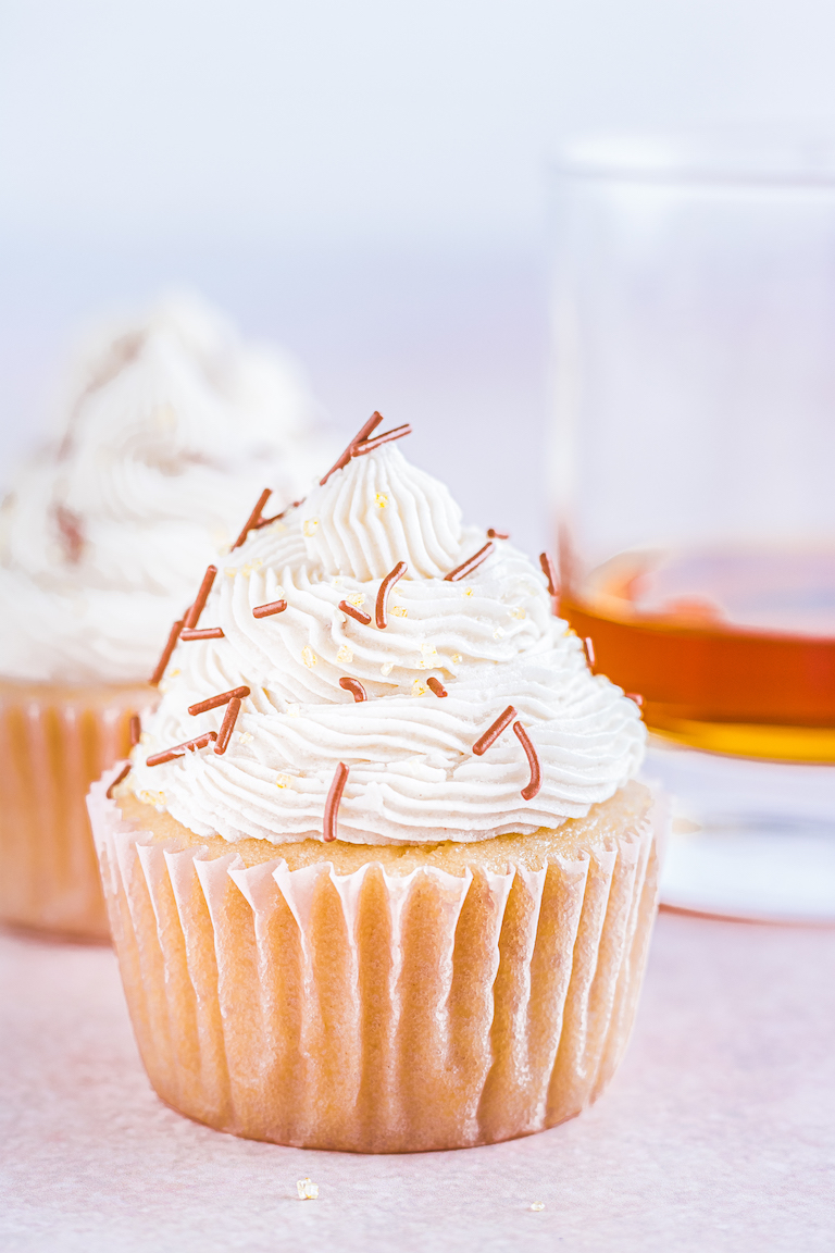 two bourbon spice cupcakes next to a glass of bourbon