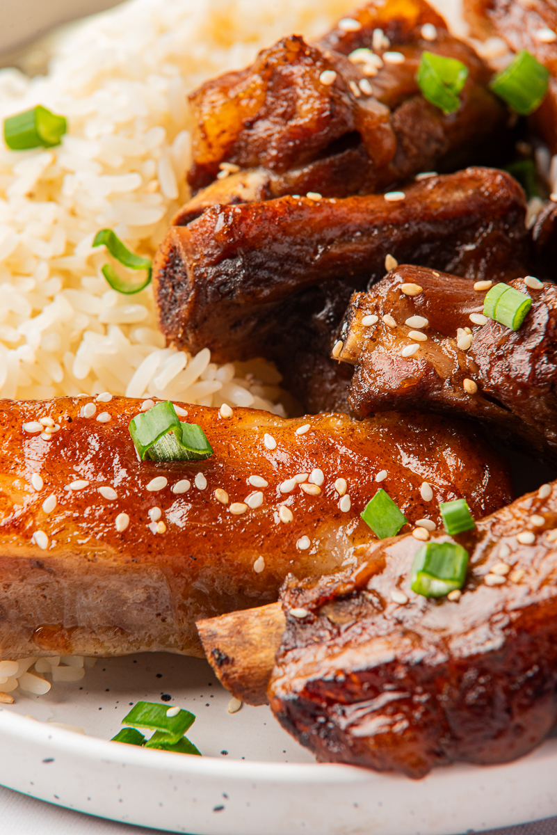 Extreme close-up of saucy pork ribs and fluffy rice, showing crispy edges, sesame seeds, and fresh green onion detail.