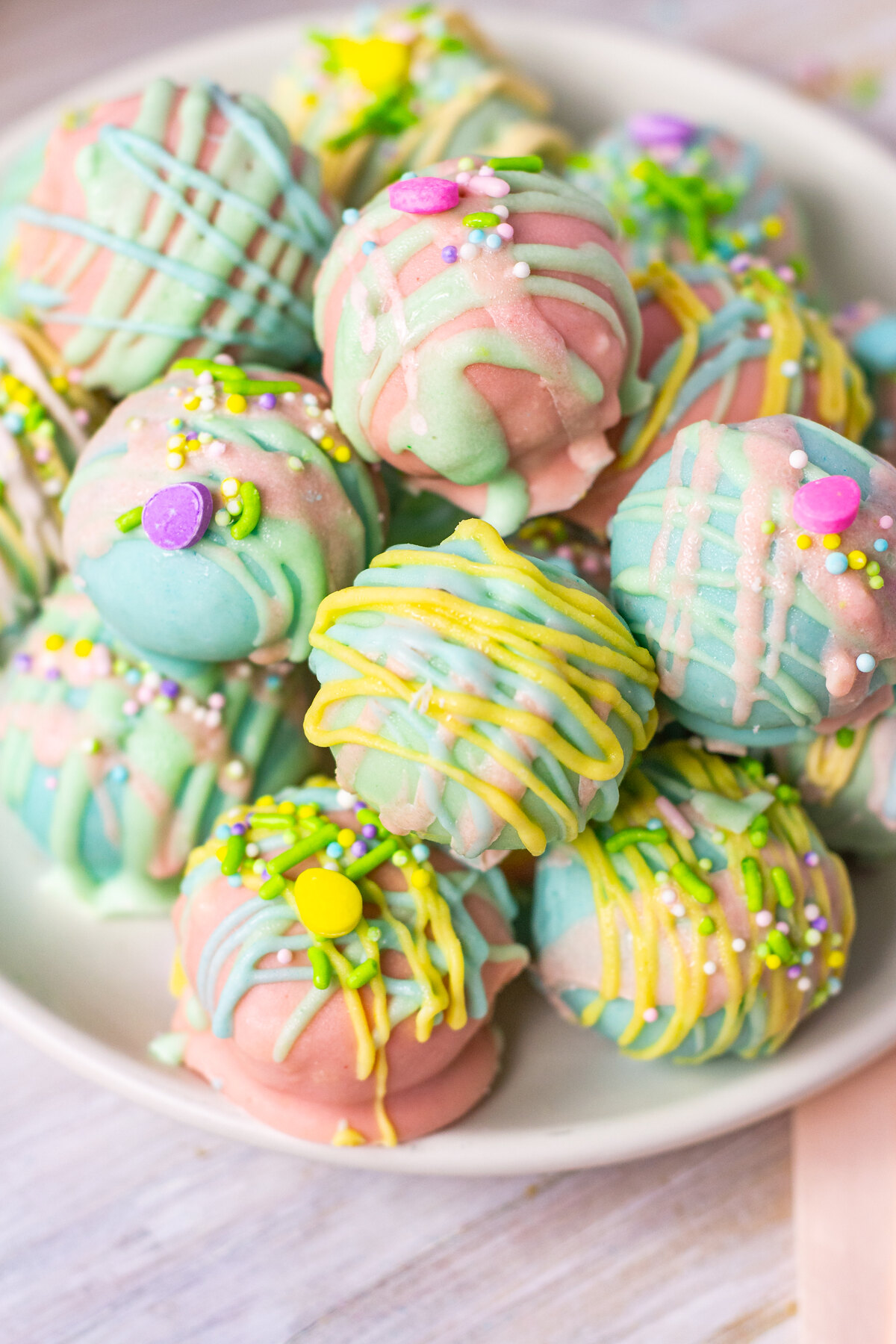 A close-up of a pile of Easter-themed Oreo truffles, coated in pastel chocolate with drizzle decorations and tiny sugar pearls and sprinkles.