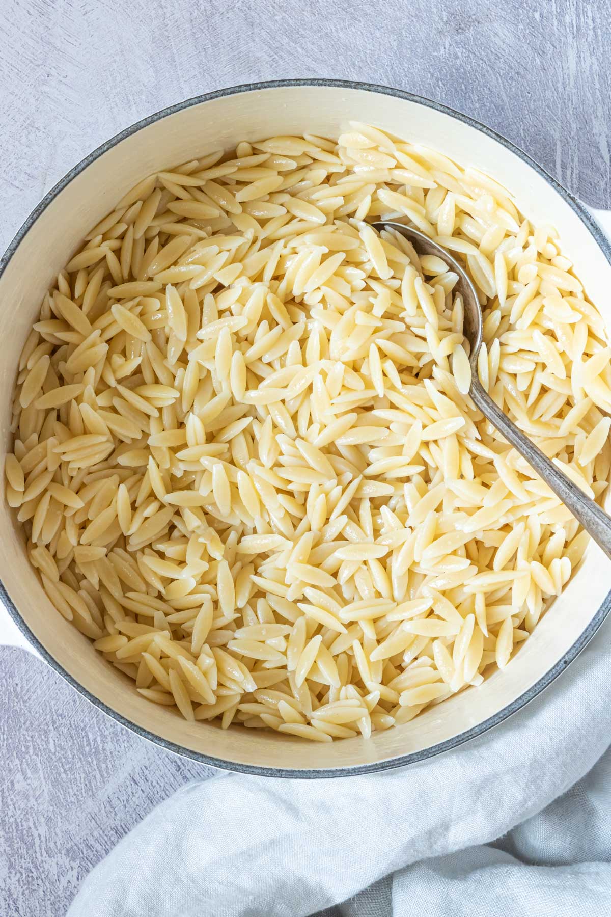 A large bowl filled with orzo with a serving spoon inside is the final result from this how to cook orzo recipe.