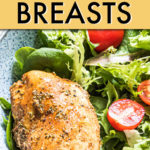 a whole cooked chicken breast resting on a salad