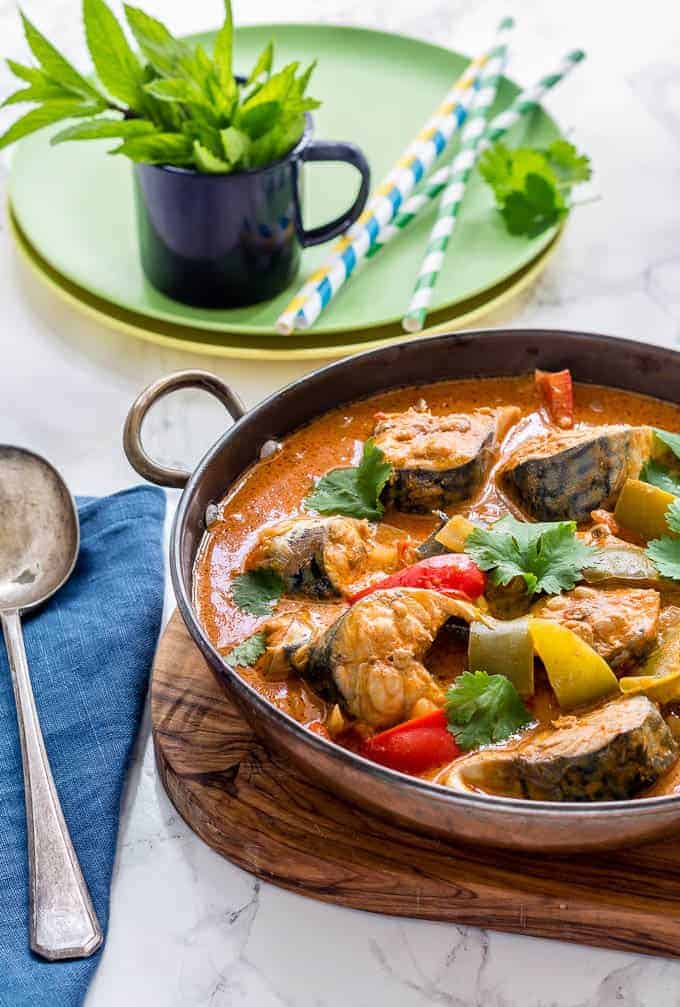 A Pot of Moqueca Baiana (Brazilian Fish Stew) with plates, spoons and straws around it