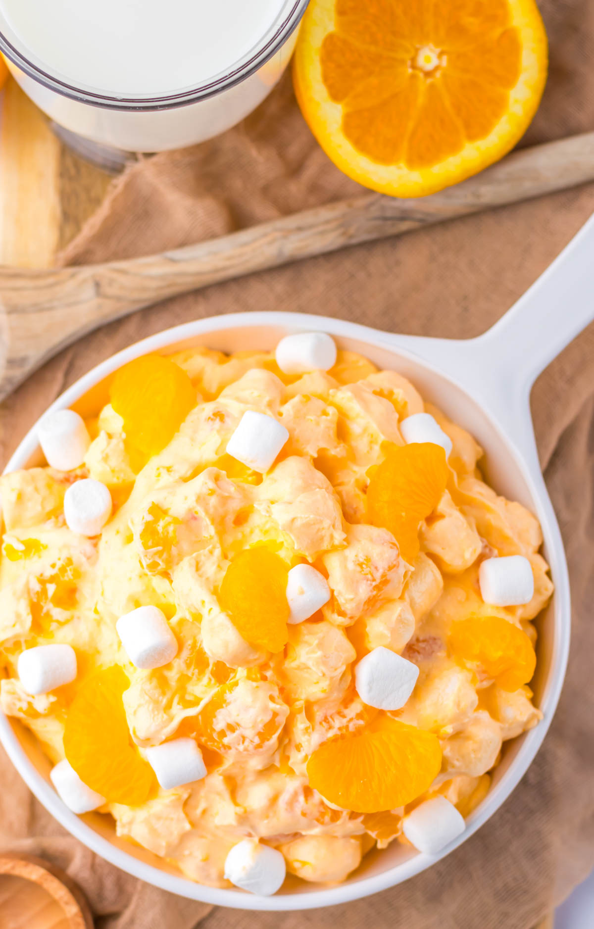 top down view of the completed orange fluff salad recipe served in a white dish and set next to half an orange.