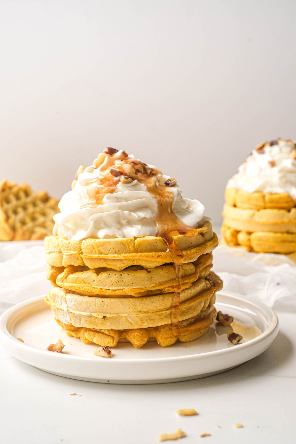 a stack of pumpkin waffles topped with whipped cream, syrup and nuts
