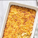 a rectangular dish of scalloped corn with a spoon in it