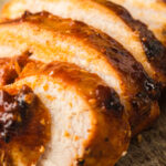 Sliced smoked chicken breast with barbecue glaze on a wooden board.