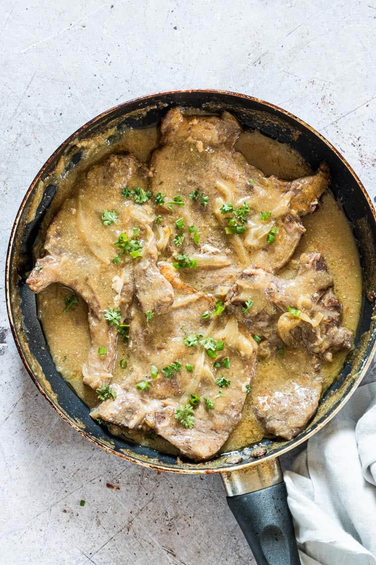 smothered pork chops in a pan and ready to serve