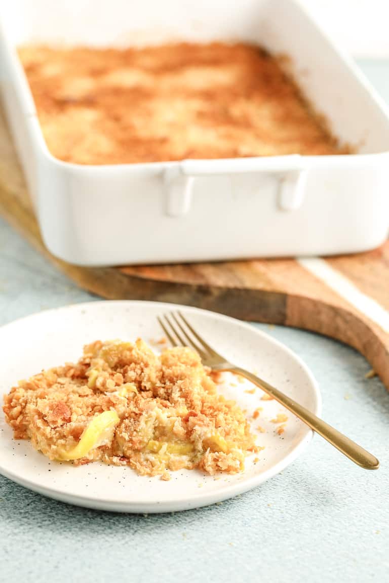 a serving of yellowe squash casserole on a white plate in front of the full casserole dish